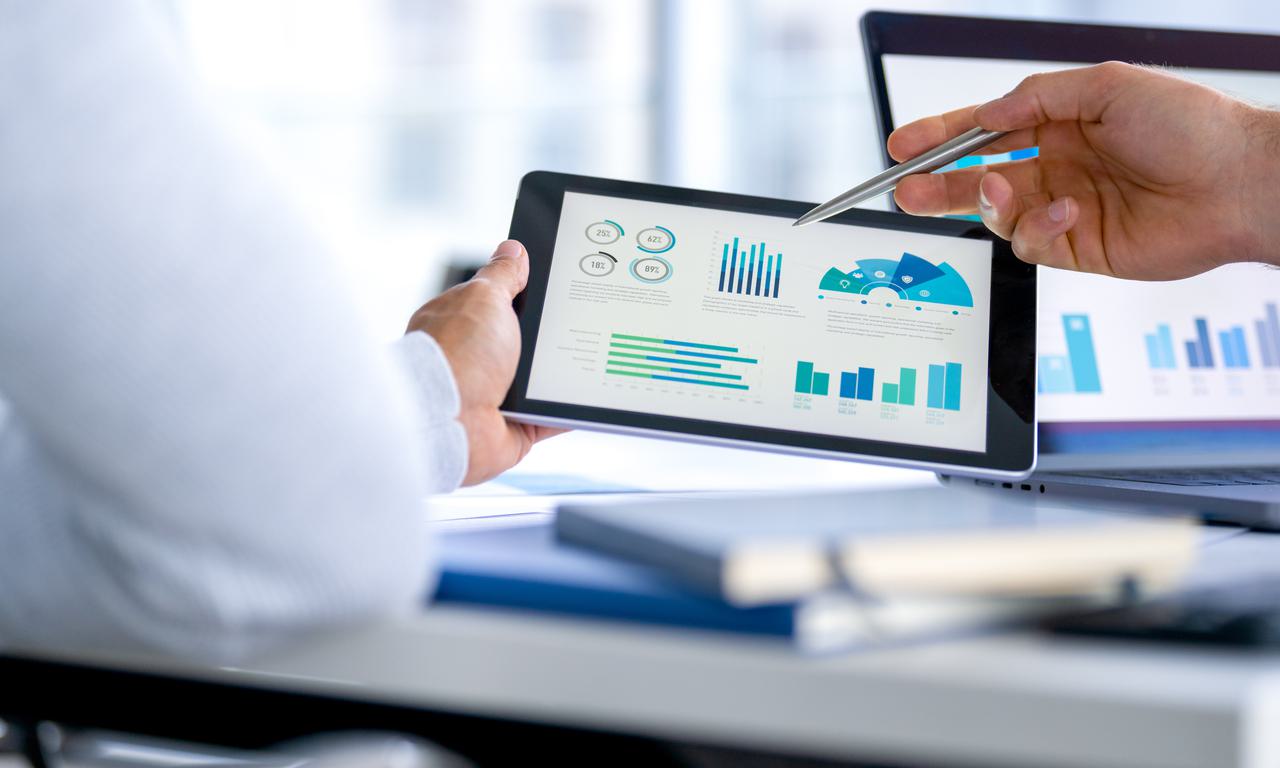 hand holding a tablet with graphs and charts while another hand points while holding a pen